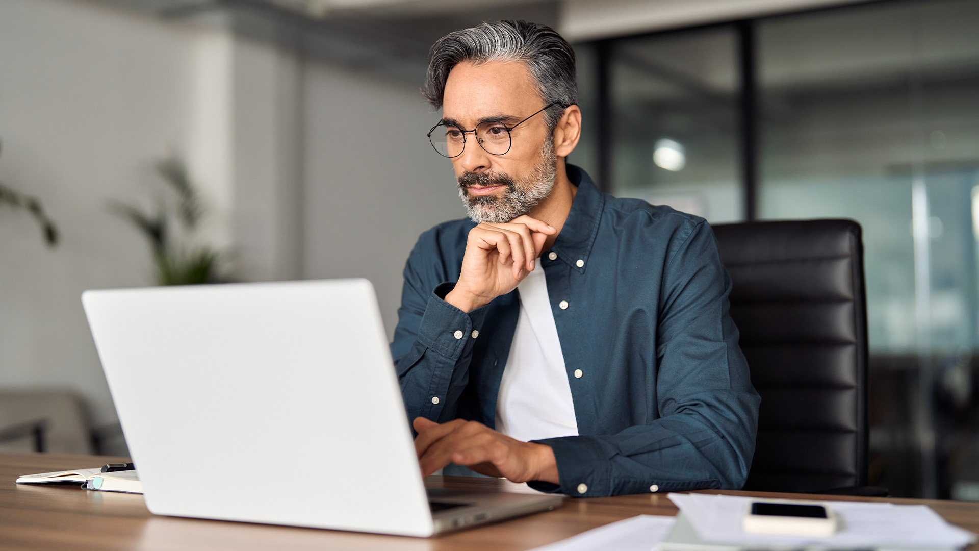Uomo adulto che guarda il suo laptop con un'espressione concentrata, leggendo una guida all'adesione al fondo pensione negoziale