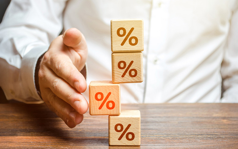 Una mano che stabilizza una pila di cubi di legno con il simbolo della percentuale, rappresentando il reintegro delle anticipazioni in Fopen.