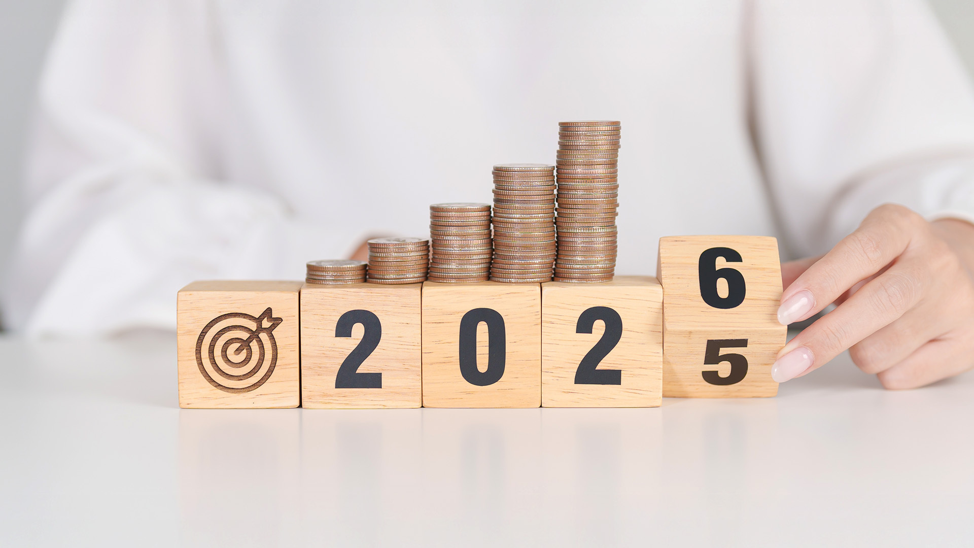 Cubi di legno che formano l'anno 2026 con pile di monete crescenti, simbolo degli aggiornamenti su Manovra 2026 e fondo pensione.