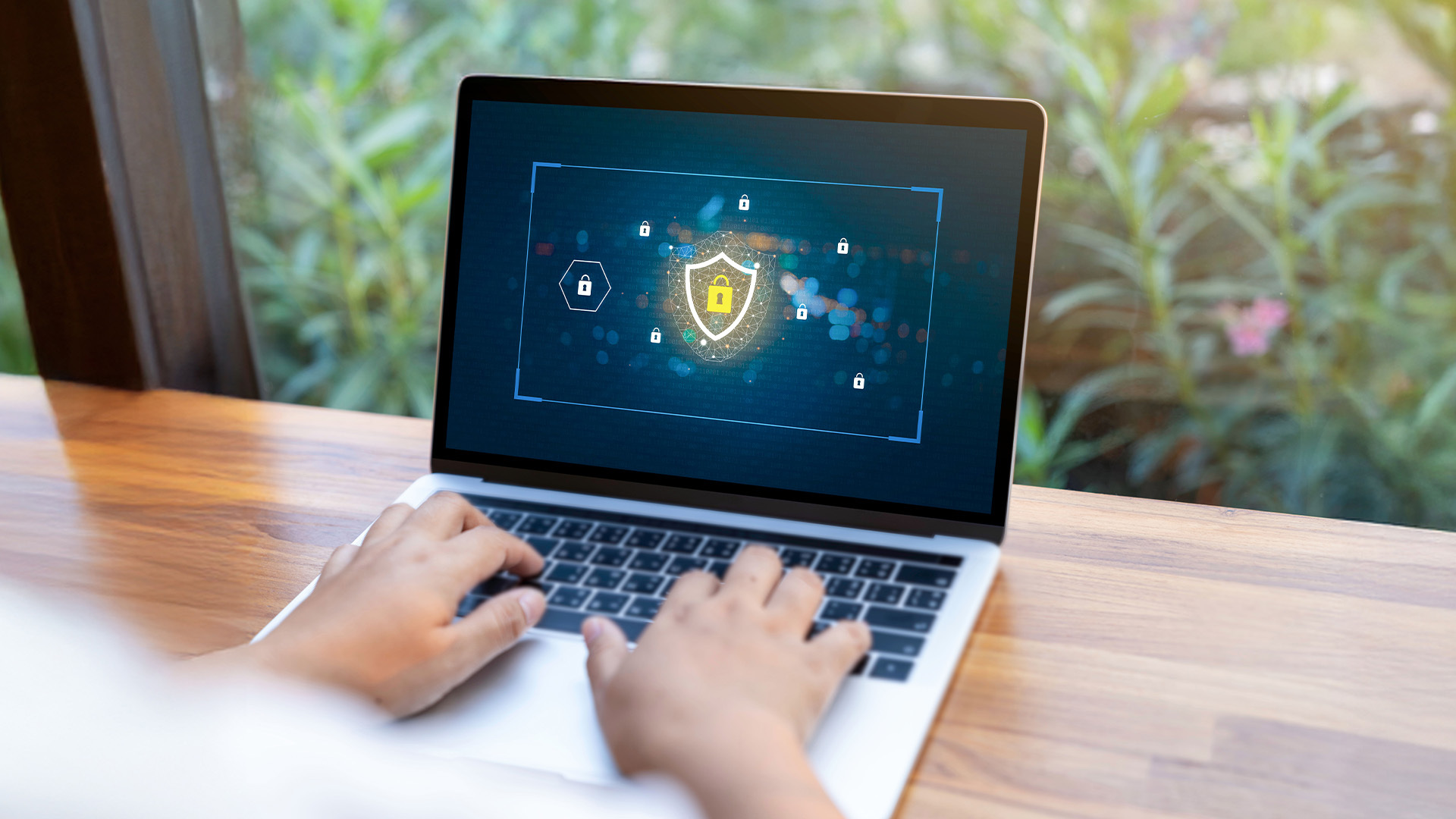 Persona che utilizza un laptop su un tavolo di legno con un'interfaccia di sicurezza digitale visualizzata sullo schermo, rappresentante la protezione dei dati personali.
